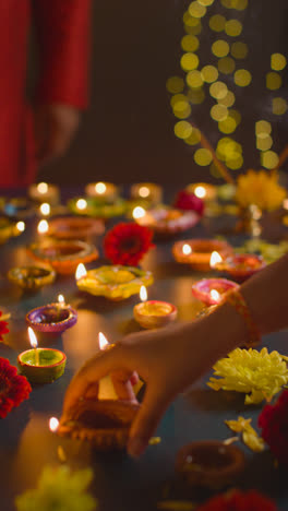 Vertical-Video-Close-Up-Shot-Of-Hands-Lighting-Diya-Oil-Lamps-Celebrating-Festival-Of-Diwali-On-Darkened-Table-2